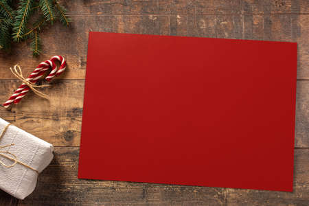 Mockup Christmas red greeting card with tree candy cane, flatlay on a rustic wooden background, with place for your text. Spruce branches on a wooden table. Ornaments for the New Year tree. Christmas concept.の写真素材
