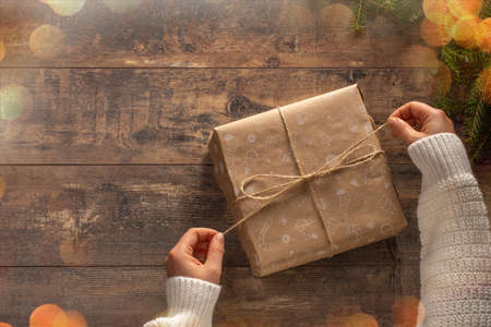 Woman hands unpacking Christmas gift box. Woman hands unpacking gift box on rustic wooden table. holiday Christmas bokeh lights.の写真素材
