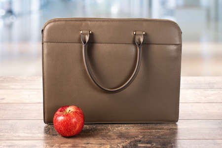 business bag, briefcase and red apple on a wooden table on a blurry background. proper nutrition at...