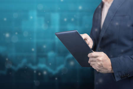 businessman holds a digital tablet on background of financial charts. Business analysis, planing and strategy concept. copy spaceの写真素材
