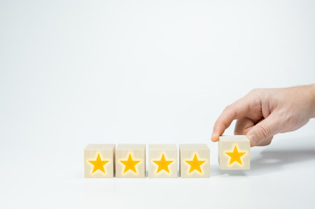 Wood cubes with gold star signs. Man Hand putting wooden five star shape on white background. Best...