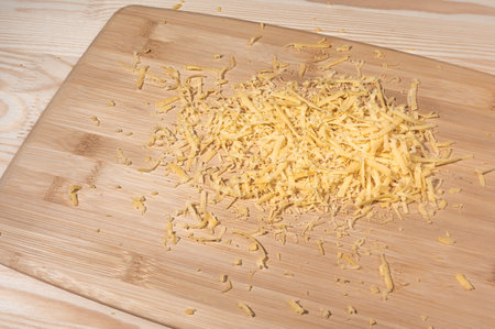 grated cheese on a wooden cutting Board. Grated cheese on the table. Pile of grated cheddar cheeseの写真素材