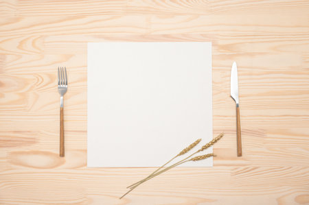 mockup Blank card and cutlery on wooden table. Top view white recipe paper page with mockup text space, invitation card and cutlery on wooden background mockup recipe paper decorated with golden earsの写真素材