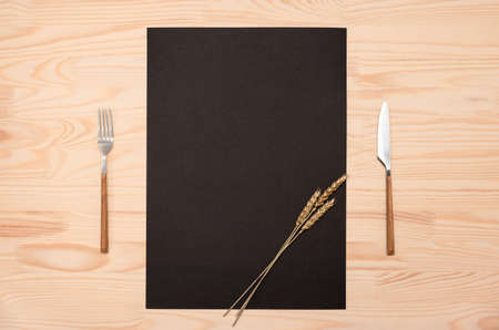 mockup Blank black card a4, a3 and cutlery on wooden table. Top view black recipe paper page with mockup text space, invitation card and cutlery on wooden background mockup recipe paper decorated with golden earsの写真素材