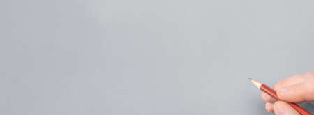 Hand with pencil writing something on gray paper. male hand is ready for drawing with red pencil. Close-up man hand writing with a pencil. banner. copy spaceの写真素材