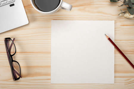 Top view paper card on office desk mockup. Blank paper on wooden desk background. desk with blank paper sheet, laptop, writing supplies and green leaves on wooden background, top viewの写真素材