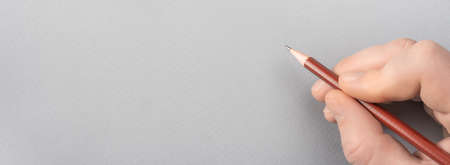 Writing on gray paper with a pencil. Hand with pencil writing something on gray paper. Human Hand Drawing With Pencil On Empty Paper Template. space for your text, message and contactsの写真素材