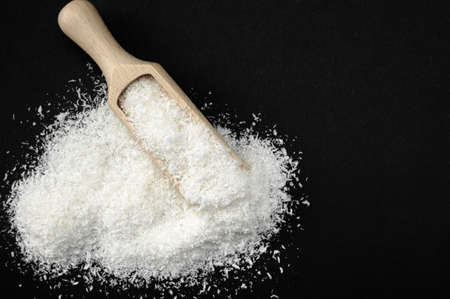 Coconut shavings. Wooden scoop Spoon with Coconut shavings on black background. copy space. Shredded coconut shavings. for cooking and spa. top viewの写真素材