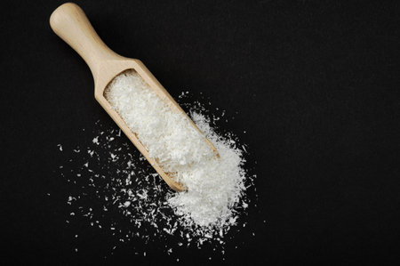 Coconut shavings. Wooden scoop Spoon with Coconut shavings on black background. copy space. Shredded coconut shavings. top viewの写真素材