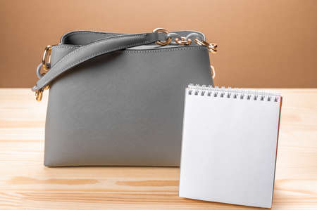 Women leather gray handbag and notepad. women's bag and Notepad for writing. concept of office work or training, education. yellow wooden table backgroundの写真素材
