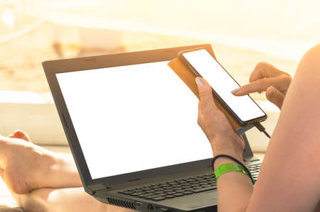 Mockup of laptop and cell phone in the hands of a woman. freelance businesswoman working on the beach using laptop and mobile phone. Vacation lifestyle communication. Freelance work conceptの写真素材