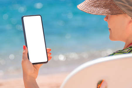 woman using smartphone sitting on a beach lounger on sea backgroundの写真素材