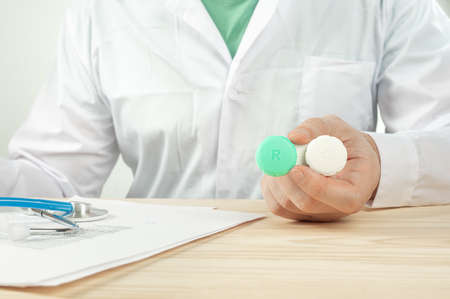 Doctor recommend contact lenses. Close-up male doctor holding pair of contact lenses. Ophthalmologist give recommendations of vision correction and eye health to patient in an optics store or clinicの写真素材
