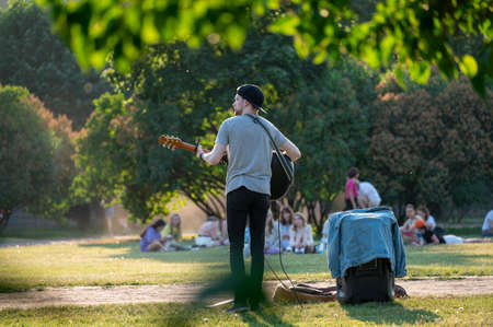 Street musician plays the guitar in the park. summer green park, rock musician gives a free concert in the park. Man in an urban park with guitarの写真素材