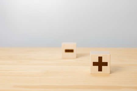 Pros and cons concept. Choosing plus with blurred minus symbol. concept of opposites, wood block with plus and minus on gray background, wooden cubes with plus and minus sign on front side. copy space.の写真素材