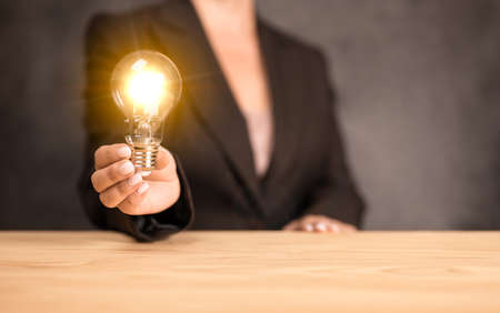 Business women holding light bulbs, new ideas with innovative technology and creativity. Woman hand holding light bulb on wooden desk. Concept new idea with innovation and creativityの写真素材