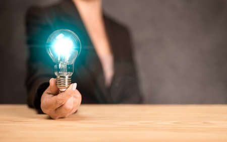 Idea concept. businesswoman holds a glowing blue light bulb. woman gave an innovative idea. Closeup image of a woman holding and showing a glowing light bulb. innovation and creativity. copy spaceの写真素材