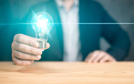 Innovative idea in businessman hand. Hand holding light bulb on wood table. Concept of inspiration...
