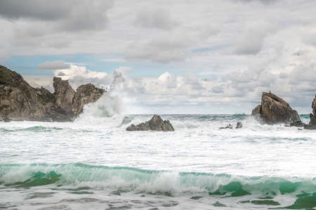 Ocean water splash on rock beach with beautiful sky and clouds. Sea wave splashing on stone at sea shore on winter. rocky coastline with white water swirling around the rocksの写真素材