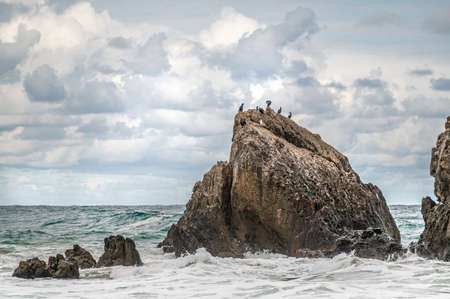 Ocean water splash on rock beach with beautiful sky and clouds. Sea wave splashing on stone at sea...