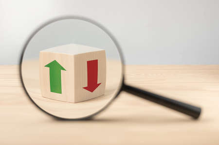 Economy growth and decline analysis. Magnifying glass and wooden cube with green and red arrow. Searching for decisions. Strategy for investors to determine chance to recover after recessionの写真素材