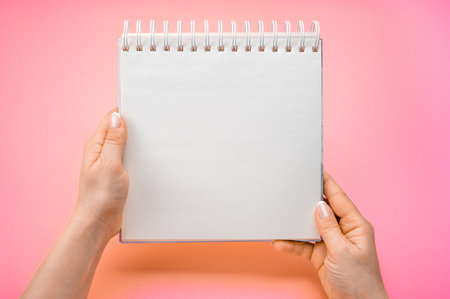 close up view female hands hold mockup notepad on pink purple background. woman holding notepad. Mockup notepad with woman hands on pink table backgroundの写真素材