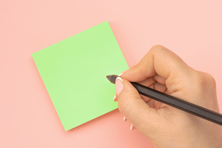 Hand written notes black pencil on green sticker. pink table background. woman hand writing on green sticky notes. Business people meeting and use notes to share idea on sticky note.の写真素材