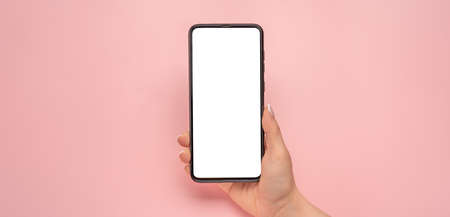 Woman hand holding black cell phone smartphone with blank white screen and modern frame less design, isolated on pink background. Mockup cell phone. female hand holding mobile phone. copy spaceの写真素材