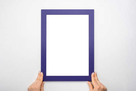 Hanging photo frame mockup on pink wall. picture frame mockup. Woman hold blank diploma frame on pink wall background. Cropped hand of woman holding picture frame against white wall. copy spaceの写真素材