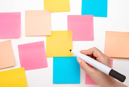 Sticky note paper mockup. Many colored empty sticker notes on white wall. hand with black marker ready to write. blank Sticker notes on white background. empty sheets for notes on bulletin boardの写真素材