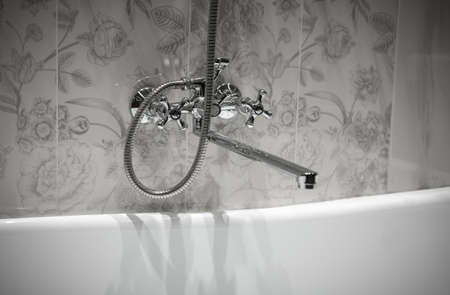 Large steel faucet mounted above bathtub. decorative tiles wall in gray tones. Bathroom water tap. faucet bathtub without waterの写真素材