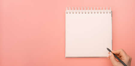 writing in blank notepad on pink background. female hands writing in mockup notepad. Woman writing in notepad. Mockup notepad with woman hands on pink table backgroundの写真素材