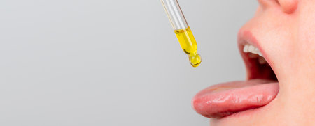 tongue oil pipette. herbal alternative medicine and dietary supplements woman taking cbd hemp oil drops in mouth from dropper. medical cannabis oilの写真素材