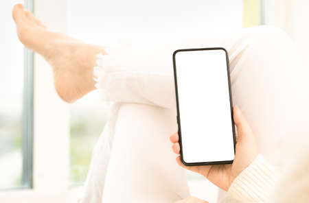 mockup image woman holding smartphone with blank white screen. Woman in white jeans sits...