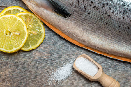 Close up Fresh raw salmon, red fish with spices, salt, lemon, pepper, rosemary on dark wooden background. Fresh raw salmon fish with spices, top view. Raw fish carcass on wood tableの写真素材