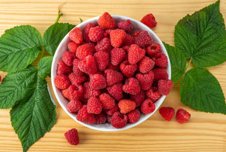Raspberries on white plate on wooden table with leaves. Organic raspberries grown without the use of...