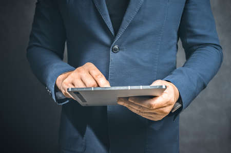 Businessman holding tablet computer on dark background. Male Businessman Programs Something while Holding Tablet Computer in His Hands. He Works in Dark Modern High-Tech Office.の写真素材