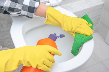 Deep cleaning service. Close up hand with detergent cleaning toilet. hands wearing yellow protect glove using liquid cleaning solution cleaning flush toilet, disinfection and hygiene conceptの写真素材