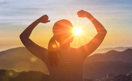 Successful woman has achieved new peak. Woman standing at top of mountain as sun begins to set. Success Business Leadership. Female silhouette on sunrise mountain backgroundの写真素材