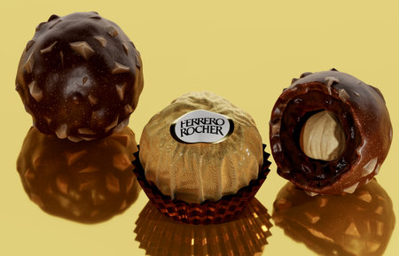 New York, USA - May 31, 2023: ferrero rocher chocolate and hazelnut confectionery. chocolate consists of whole roasted hazelnut. golden mirror background. sweet is produced by machinery.のeditorial素材