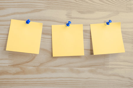 Three yellow paper notes mockup pinned to wooden bulletin board. sticky notes on bulletin board. Three sticker with push pins on wooden backgroundの写真素材