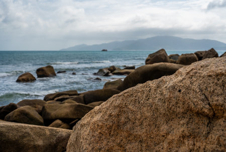 seascape of coastal panorama. Monumental granite boulders stand resilient against crashing waves, set beneath dramatic, cloud-filled sky. landscape captivates with its vastness and natural spectacleの写真素材