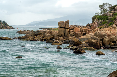 seascape of coastal panorama. Monumental granite boulders stand resilient against crashing waves, set beneath dramatic, cloud-filled sky. landscape captivates with its vastness and natural spectacleの写真素材