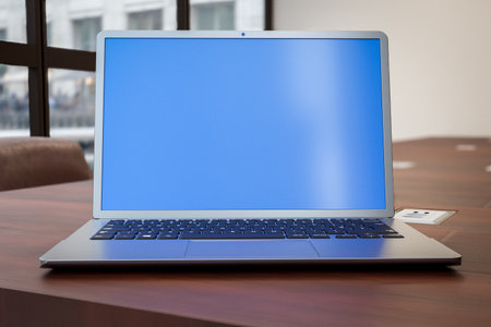 Laptop mock up with blue blank screen on wooden table with light beams empty space. laptop and studying, office concept, empty brown table stage with laptopの写真素材