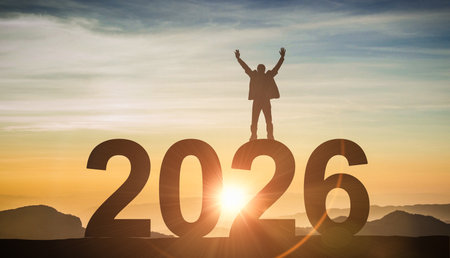 Man on top of 2026 text with arms up. Symbolizes reaching goals, personal success, new year's resolutions, and future achievementsの写真素材
