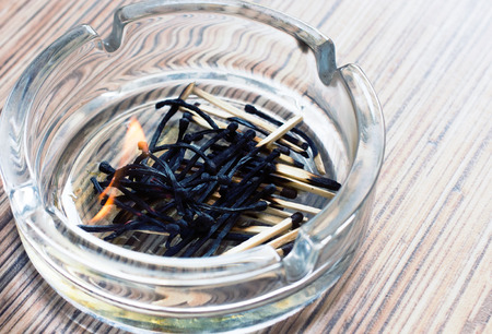burnt safety matches in a glass ashtray on wooden background texture