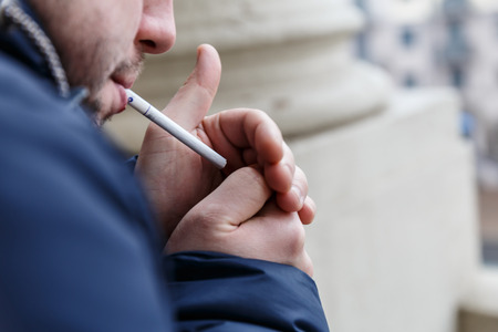 man with stubble lights a cigarette and smokesの写真素材