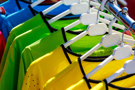 Baby clothes pants t-shirts sweaters shirts hanging on hangers in a shop outside in sunny weatherの写真素材