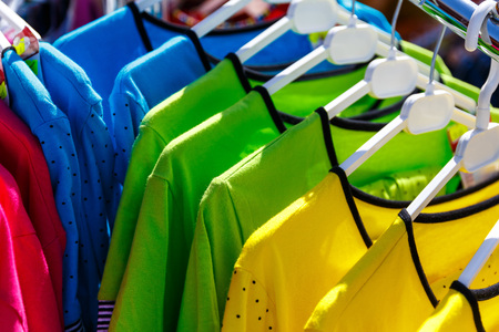 Baby clothes pants t-shirts sweaters shirts hanging on hangers in a shop outside in sunny weatherの写真素材