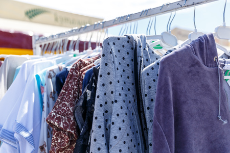 Baby clothes pants t-shirts sweaters shirts hanging on hangers in a shop outside in sunny weatherの写真素材